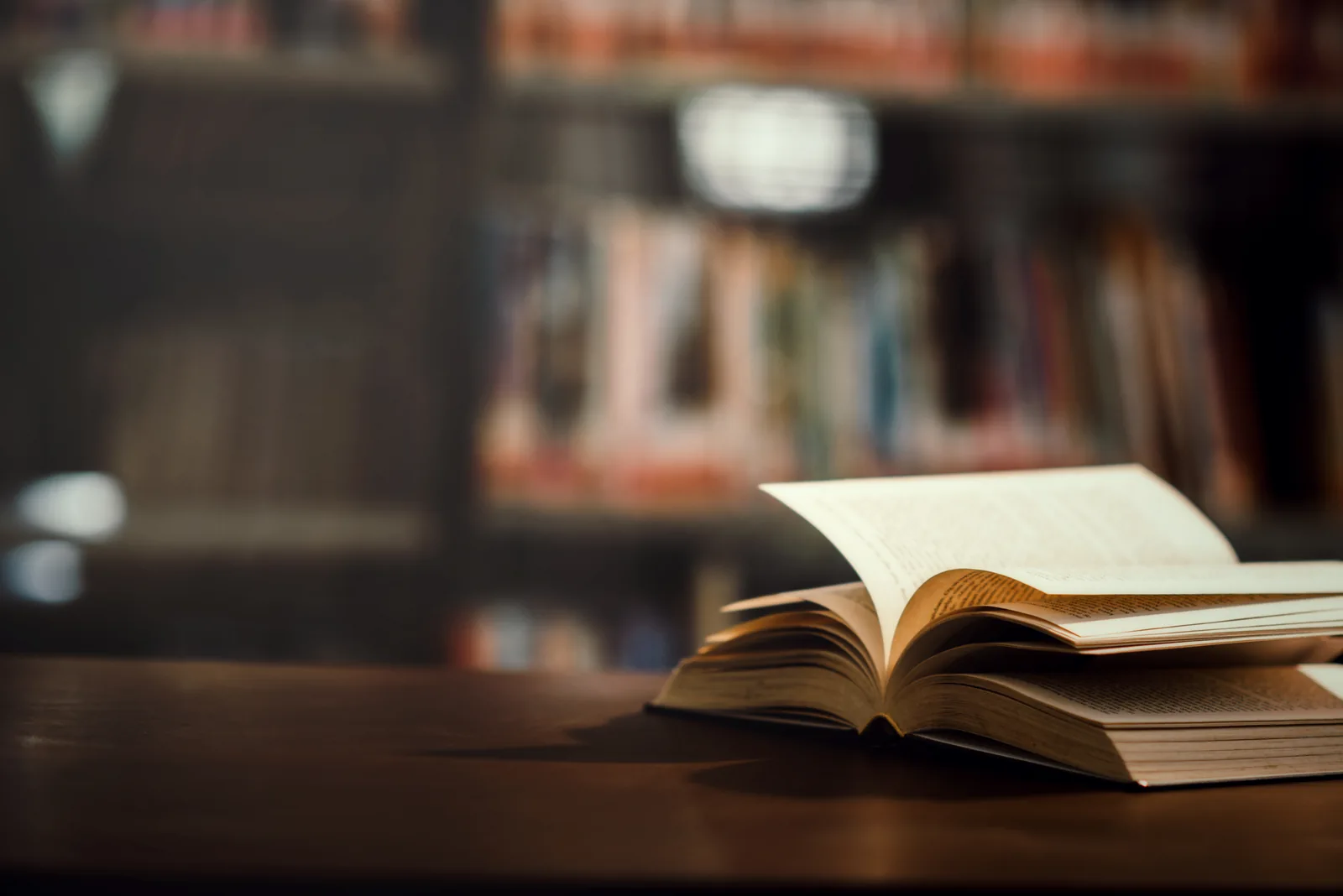 Livro aberto sobre uma mesa com estantes de biblioteca ao fundo