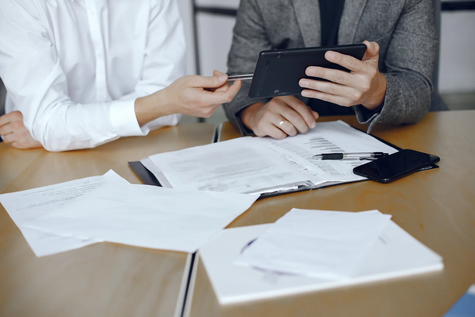 Profissionais analisando documentos e consultando um tablet à mesa
